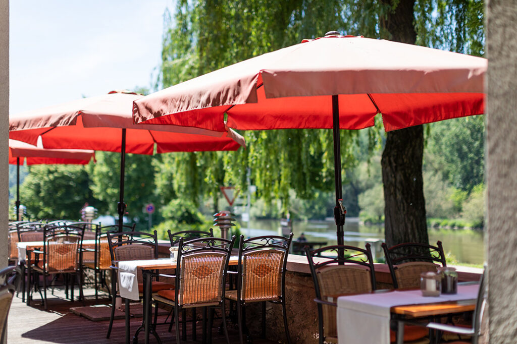 Rote aufgespannte Sonnenschirme stehen neben den eingedeckten Tischen auf der Terrasse des Restaurants Karlstadt